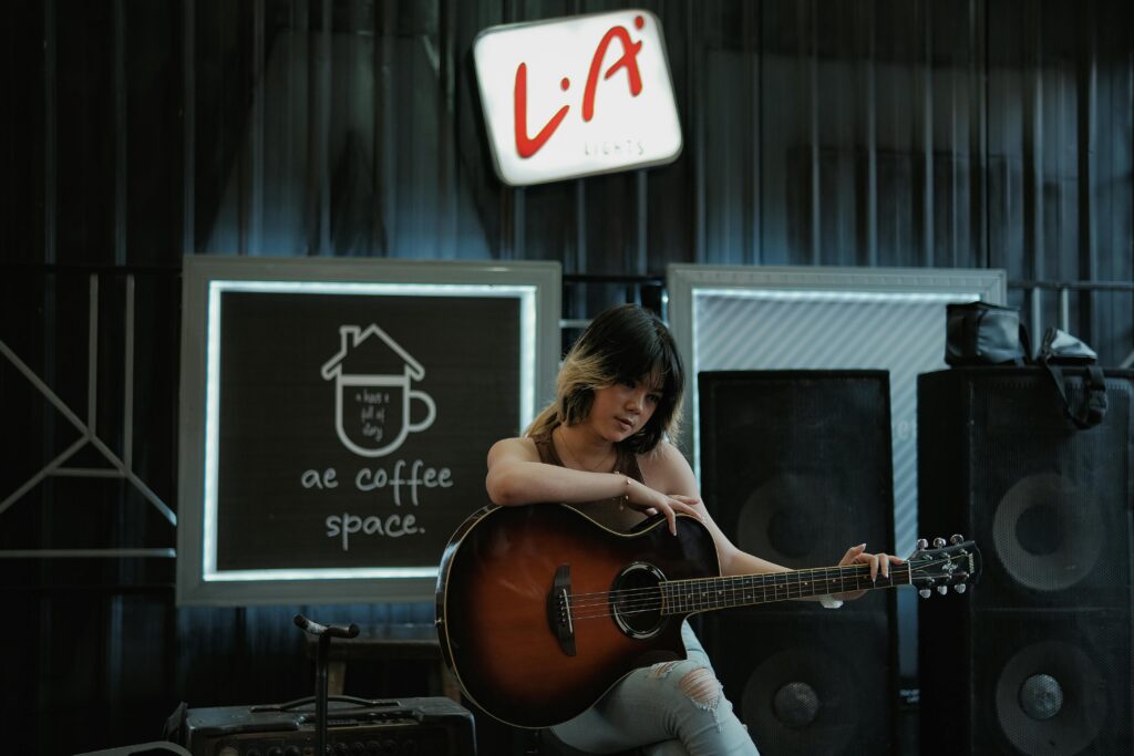 Asian woman playing guitar in a stylish indoor coffee space, showcasing musical passion.