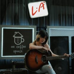 Asian woman playing guitar in a stylish indoor coffee space, showcasing musical passion.