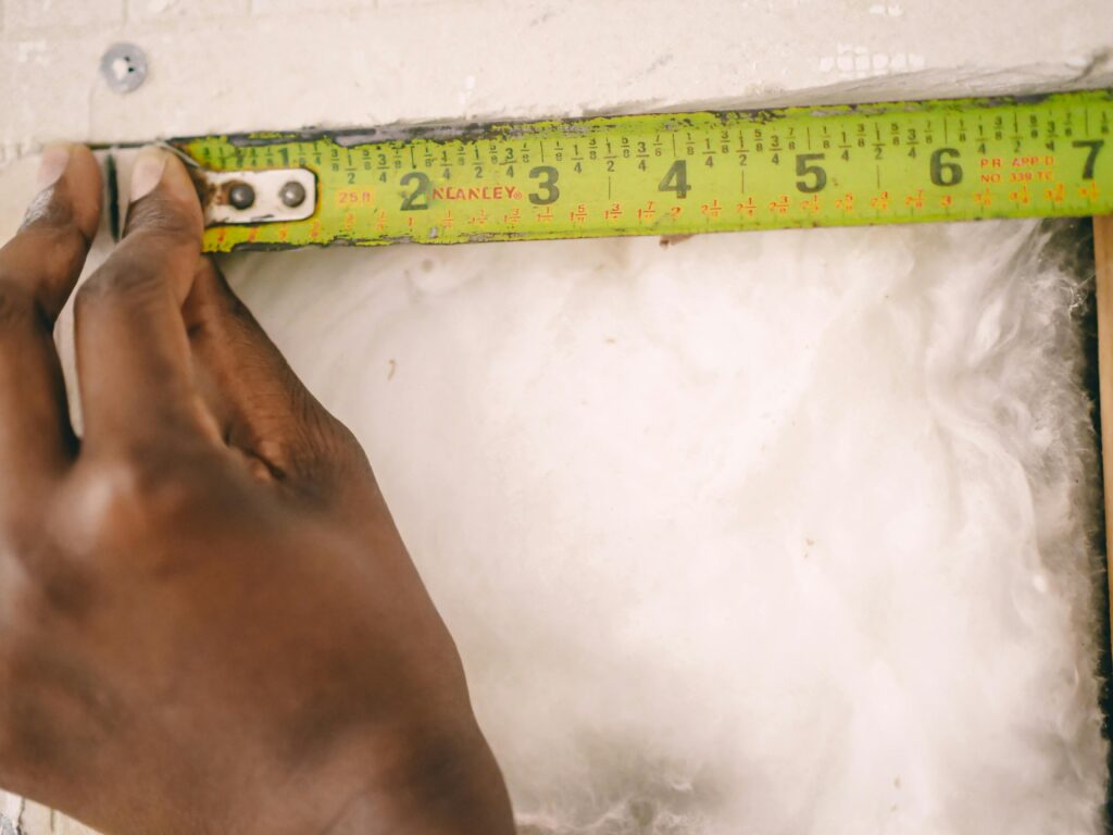 Close-up of a hand measuring insulation with a yellow tape measure.