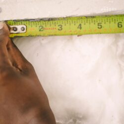 Close-up of a hand measuring insulation with a yellow tape measure.